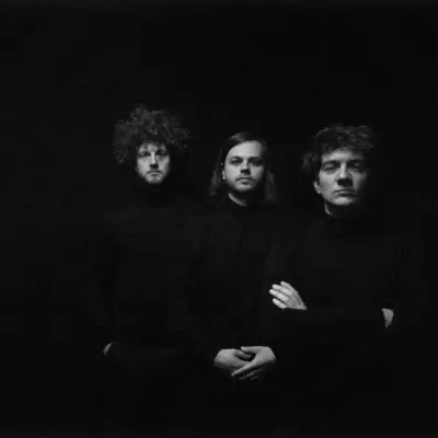 Monochrome press photo of Daniel Klein's project "Loom and Thread" – three figures in black, emerging from the shadows.